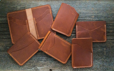 Collection of various wallets in English Tan Horween Dublin leather randomly arranged on a weathered barn board