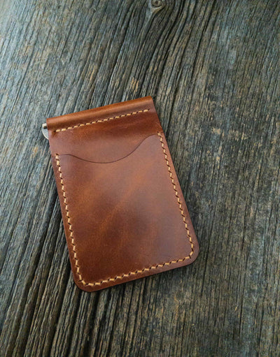 Folding Clip Wallet in Buck Brown full grain traditional harness leather, pockets hand stitched with Ritza Tiger thread in Tan, and brass spring clip. Sitting angled on old barn board.