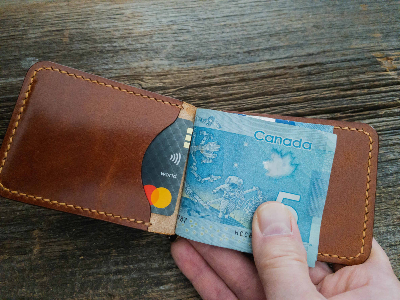 Folding Clip Wallet in Buck Brown full grain traditional harness leather, hand stitched with Ritza Tiger thread in Tan. Held open in a hand. Wallet holding cash and credit card. 